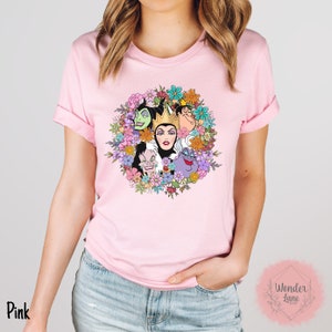 May include: Pink t-shirt with a floral wreath design featuring the faces of Disney villains Maleficent, Cruella de Vil, Ursula, and the Evil Queen.
