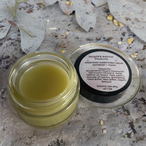 May include: A small glass jar of green salve with a black lid. The lid has a label that reads "Jacquie's Natural Products Handmade Everything Salve Dandelion + Monoi" and lists the ingredients: "Dry Dandelion Flowers (taraxacum officinaleni) infused in Monoi Tahitian Oil (monoi tiare tahiti). Avocado Oil (persea, gratissima). Monoi Butter, Shea Butter, Organic Beeswax" and "External Use Only wt 1 oz".