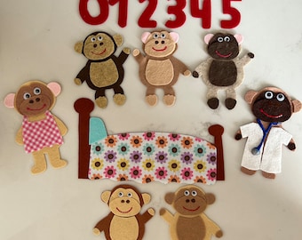 May include: Felt toy set featuring a bed, 6 monkeys, and the numbers 0-5. The monkeys are brown, tan, and gray with different facial expressions. The bed is blue and white with a floral pattern.