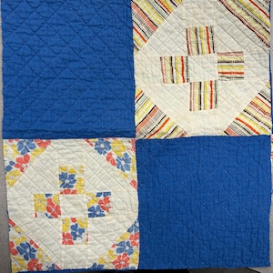 May include: A blue and white patchwork quilt with a diamond pattern. The quilt is made of different fabrics with floral and striped designs.