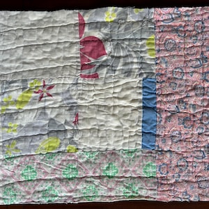 May include: A patchwork quilt with various fabric patterns. The quilt features sections of white, floral, and paisley prints in shades of pink, blue, green, and gray. The quilt is hand-stitched with horizontal lines across the surface.