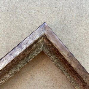 May include: Close-up of a corner of a wood picture frame with a distressed, dark brown finish.