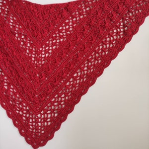 May include: A red crocheted shawl with a delicate lace pattern. The shawl is triangular in shape and has a scalloped edge.