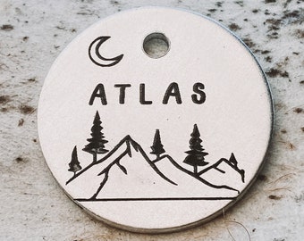 May include: A silver round tag with a crescent moon, the word "ATLAS" and a mountain range with trees.