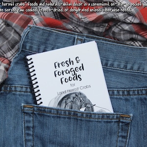 May include: A small, white spiral bound book with the title "Fresh & Foraged Foods for Land Hermit Crabs". The book is in the back pocket of a pair of blue jeans.