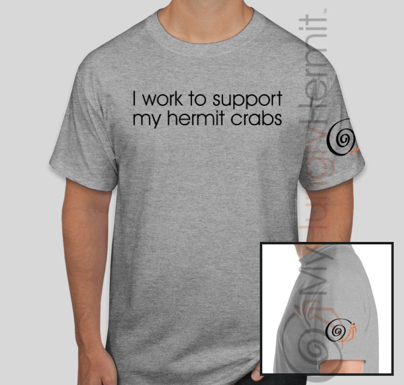 May include: A heather gray short-sleeve t-shirt featuring the black text "I work to support my hermit crabs" printed on the chest. The left sleeve displays a small black and orange spiral shell graphic, which is also visible in the inset image.