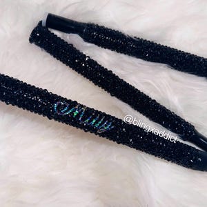 May include: A folding mobility cane covered in small black crystals. The cane features the name Emily spelled out in iridescent crystals on the shaft. The text @blingxaddict is printed in white near the center of the cane's handle section.