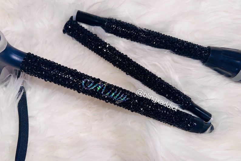 May include: A folding mobility cane covered in small black crystals. The cane features the name Emily spelled out in iridescent crystals on the shaft. The text @blingxaddict is printed in white near the center of the cane's handle section.