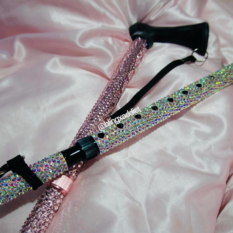 May include: A walking cane featuring a black handle and a shaft covered in pink rhinestones, paired with a second cane shaft adorned with iridescent crystals and black accents. The text @blingxaddict is visible on the iridescent cane surface.