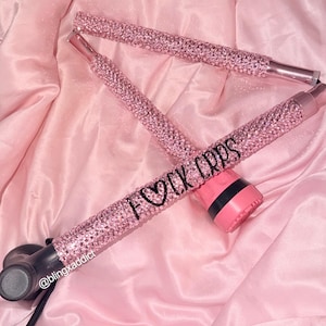 May include: A folding mobility cane covered in light pink rhinestones. The handle section features the black text F&hearts;CK CRPS. The cane has a black base and a black handle grip. The design includes a small black text label reading @blingxaddict.
