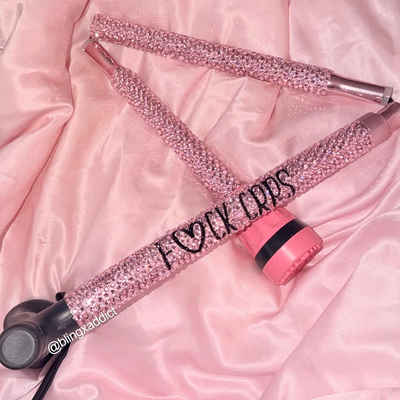 May include: A folding mobility cane covered in light pink rhinestones. The handle section features the black text F&hearts;CK CRPS. The cane has a black base and a black handle grip. The design includes a small black text label reading @blingxaddict.