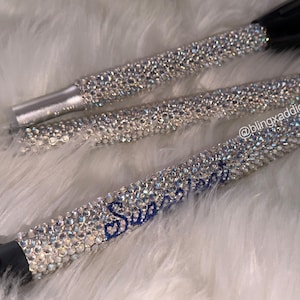 May include: Three cylindrical flashlights covered in clear, reflective rhinestones. The handle of the bottom flashlight features the blue cursive text "Sweetheart" and the handle of the middle flashlight displays the text "@blingxaddict".