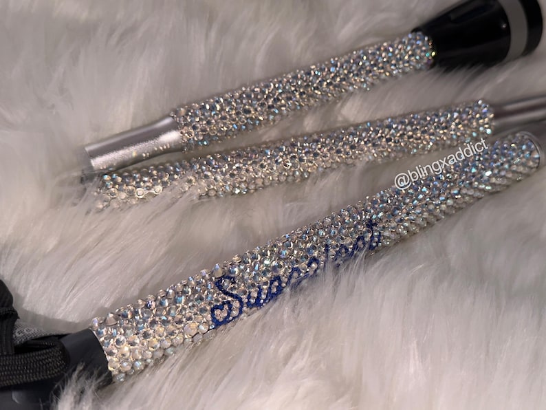 May include: Three cylindrical flashlights covered in clear, reflective rhinestones. The handle of the bottom flashlight features the blue cursive text "Sweetheart" and the handle of the middle flashlight displays the text "@blingxaddict".