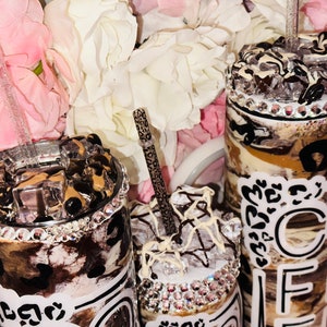 May include: Three stainless steel tumblers with lids and straws. The tumblers are decorated with a brown and white marble pattern, black leopard print, and white text that says "Coffee". The tumblers are adorned with rhinestones.