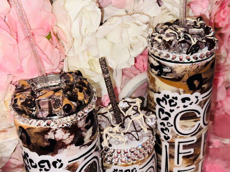 May include: Three stainless steel tumblers with lids and straws. The tumblers are decorated with a brown and white marble pattern, black leopard print, and white text that says "Coffee". The tumblers are adorned with rhinestones.