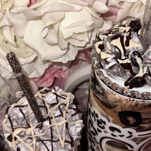 May include: Two personalized coffee tumblers with a brown and white leopard print design. The tumblers are decorated with white and brown chocolate and topped with clear plastic ice cubes. One tumbler has a straw with a leopard print design.