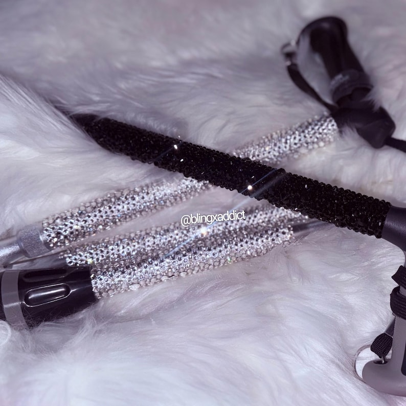 May include: Two walking canes featuring shafts covered in sparkling crystals. One cane is adorned with clear, reflective crystals, while the other is covered in black crystals. Both canes have black handles and the text @blingxaddict is visible.