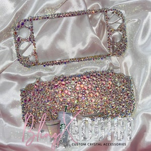 May include: A clear plastic case with a sparkly pink and white crystal design. The case is for a Nintendo Switch console. The text "Bling Addict Custom Crystal Accessories" is at the bottom of the image.