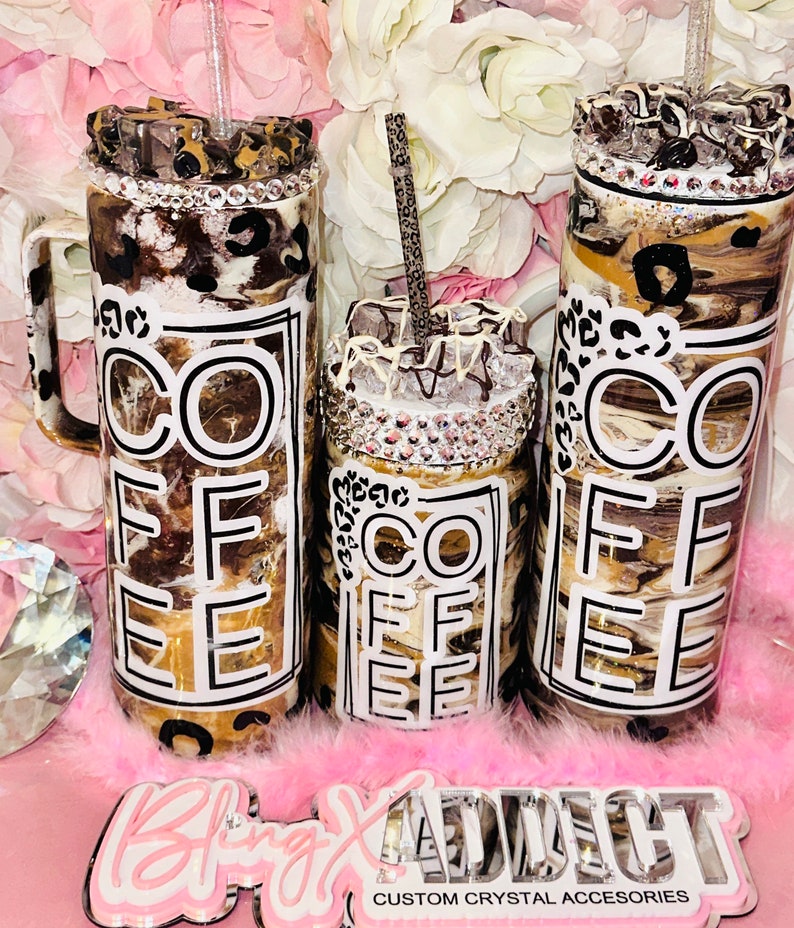 May include: Three stainless steel tumblers with a brown and white marble design and a black and white "COFFEE" graphic. The tumblers have a clear lid and a straw. The tumblers are sitting on a pink fluffy surface.