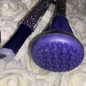 May include: A purple crutch tip with a textured circular base and a dark purple shaft covered in shimmering dark purple crystals. The shaft features the text @blingxaddict printed in white. The design includes a light gray circular end cap.