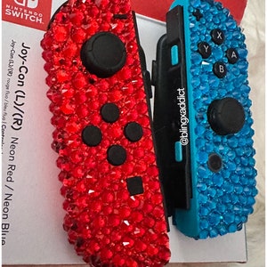 May include: A pair of Nintendo Switch Joy-Con controllers, one red and one blue, covered in rhinestones. The red controller has the text "Joy-Con (L)/(R) Neon Red / Neon Blue" and "Joy-Con (L)/(R) rouge fluo/bleu fluo | Control." The blue controller has the text "@blingxaddict".
