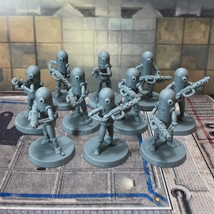May include: A collection of nine unpainted grey plastic miniature robot figures, each featuring a cylindrical head with a single central eye, thin articulated limbs, and a round base, with each figure holding a detailed futuristic blaster rifle.