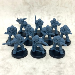 May include: Ten grey miniature soldier figurines, each on a black circular base. The soldiers are armed with rifles and other weapons, and wear armour and helmets. The figurines are arranged in a group, suitable for tabletop gaming.