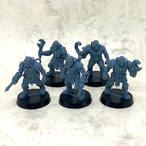 May include: Six grey miniature figurines of armored figures, each on a black circular base. The figures are holding tools and weapons, including wrenches and bladed instruments. The background is a light grey.