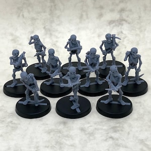 May include: A set of twelve grey plastic skeleton figurines, each holding a weapon, standing on black circular bases.