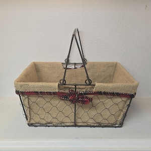 May include: A rectangular wire basket with a burlap liner and a metal handle. The basket has a chicken wire design and is trimmed with a red and black plaid ribbon. The handle is made of dark metal.