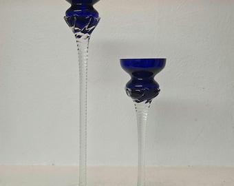 May include: Two glass candle holders. The candle holders have a clear, slender stem and a round base. The top of the candle holders are a deep blue color. One candle holder is taller than the other.