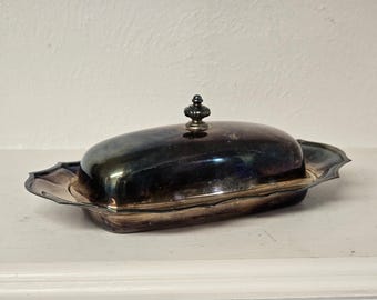 May include: A silver butter dish with a domed lid and a decorative knob. The dish has a scalloped edge and a shiny finish.