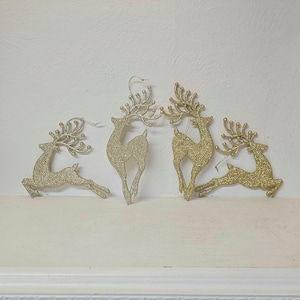 May include: Five gold glitter reindeer ornaments with silver hanging strings. The reindeer are in various poses, some standing and some lying down. The ornaments are for Christmas decorations.