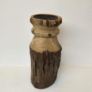 May include: A wooden candle holder with a dark brown finish and a natural wood grain. The holder has a cylindrical shape with a wide base and a narrow top. The top of the holder has a circular opening for a candle.