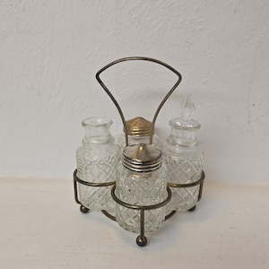 May include: A vintage condiment set featuring four clear glass bottles with diamond-patterned detailing. The bottles are held in a decorative metal stand with a handle. The set includes a salt shaker and a pepper shaker.