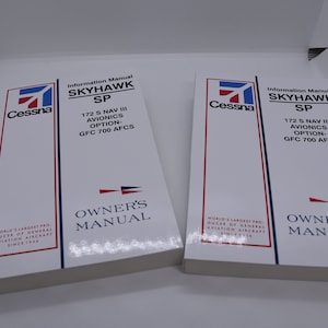 May include: Two white Cessna Skyhawk SP aircraft owner's manuals with the text "Information Manual Skyhawk SP 172 S NAV III Avionics Option- GFC 700 AFCS" and "Owner's Manual" printed on the front covers.