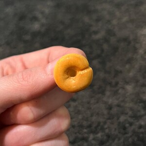 May include: A close-up of a small, round, yellow donut with a hole in the center.