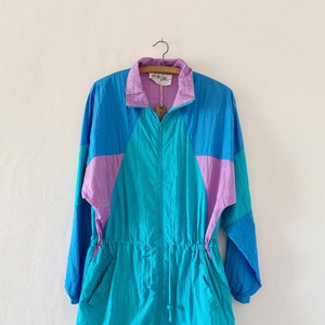 May include: A turquoise, purple, and blue color block windbreaker jacket with a drawstring waist and zipper closure.