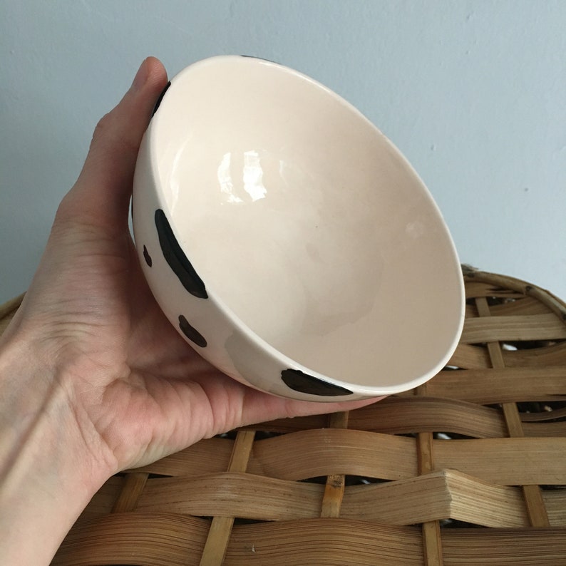 May include: A white ceramic bowl with black spots. The bowl is being held in a hand.