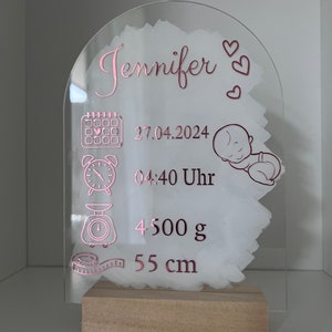 K&ouml;nnte beinhalten: Eine transparente Acryl-Plakette mit einer pinkfarbenen Inschrift, die "Jennifer" lautet und Kalender-, Uhr-, Waagen- und Ma&szlig;band-Symbole enth&auml;lt. Die Plakette enth&auml;lt auch das Datum "27.04.2024", die Uhrzeit "04:40 Uhr", das Gewicht "4500 g" und die Gr&ouml;&szlig;e "55 cm".