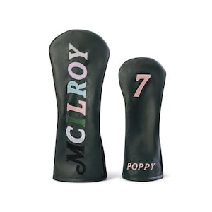 Könnte beinhalten: Zwei dunkelgrüne Golfschlägerhauben. Die größere Haube zeigt den vertikalen Schriftzug MCILROY in mehrfarbig gestickten Buchstaben. Die kleinere Haube zeigt die Zahl 7 in Rosa und das Wort POPPY in Rosa am unteren Rand.
