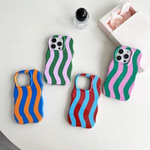 Puede incluir: Cuatro fundas de teléfono coloridas con diseños de rayas onduladas. Las fundas presentan rayas azules y naranjas, verdes y rosas, rojas y azules y verdes y rosas. Las fundas están sobre una superficie blanca.