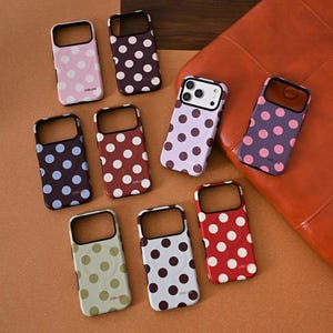 Könnte beinhalten: Eine Sammlung von Handyhüllen in verschiedenen Farben, jede mit einem Polka-Dot-Muster verziert. Die Hüllen haben einen Ausschnitt für die Kamera und sind auf einer braunen Oberfläche angeordnet. Die Hüllen sind in Rosa-, Lila-, Rot- und Grüntönen gehalten.