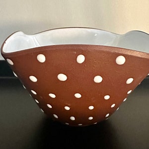 May include: A brown ceramic bowl with white polka dots. The bowl has a white rim and a slightly flared lip.