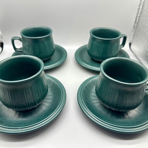 Könnte beinhalten: Set aus vier grünen Teetassen und Untertassen mit einem strukturierten Design. Die Tassen und Untertassen sind in einem tiefen Grün gehalten.