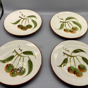 Puede incluir: Juego de cuatro platos de postre de cerámica blanca con borde marrón. Cada plato presenta un diseño pintado a mano de hojas verdes y cerezas marrones.