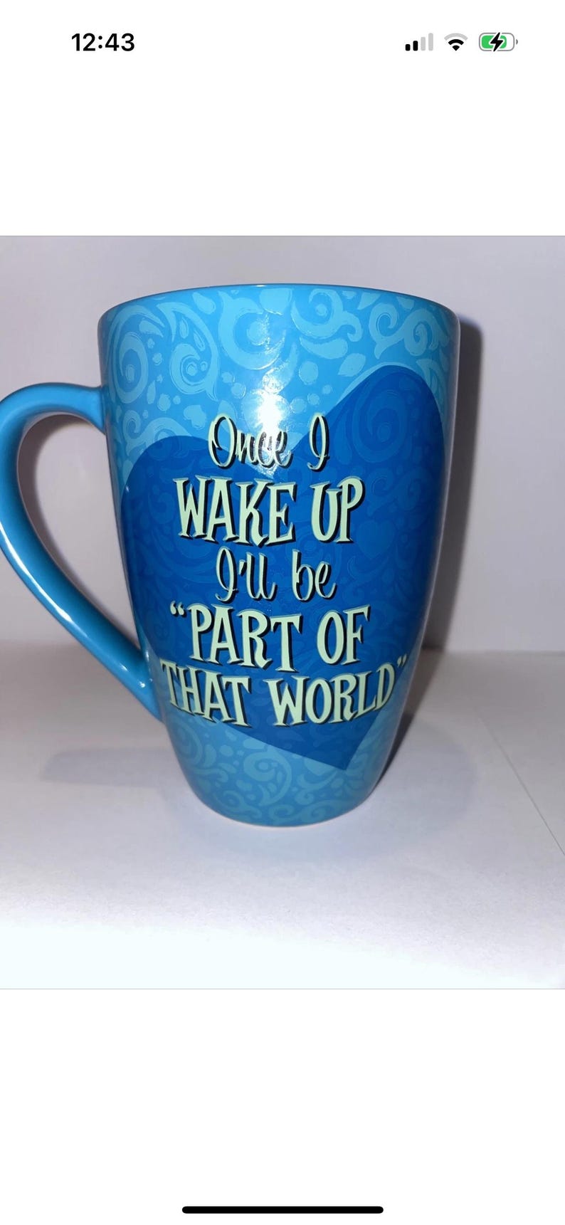 May include: A light blue ceramic mug with a handle. The mug features the text "Once I wake up I'll be 'PART OF THAT WORLD'" in white, with a decorative swirl pattern. The mug is a standard size for coffee or tea.