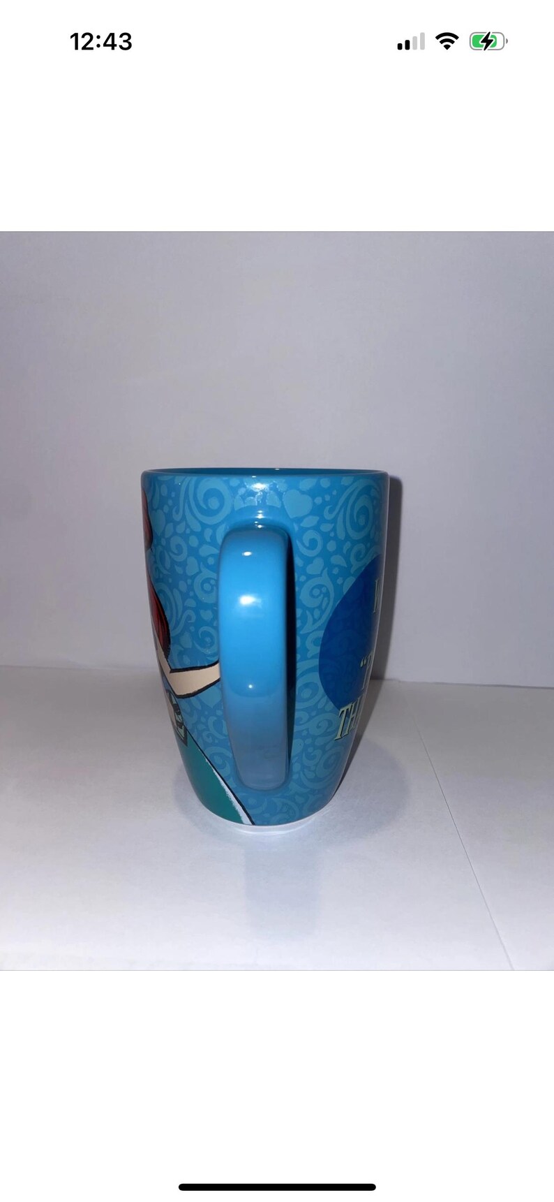 May include: A blue ceramic mug with a curved handle. The mug features a cartoon character design and the text "Thank You". The mug has a light blue handle and a patterned background.