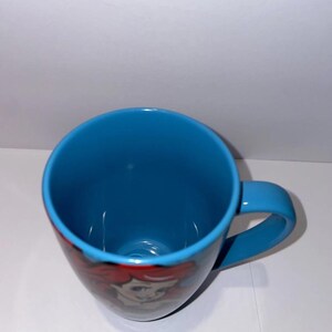 May include: A blue ceramic mug with a matching handle. The mug features a colourful illustration of a character from a popular animated film. The interior of the mug is also blue.