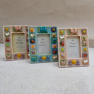 May include: Three rectangular picture frames in light pink, light blue, and light pink. Each frame features small, colorful, raised decorative squares with motifs of rabbits, carrots, bows, and stars. The center displays text: The Unique Collection 2" x 3" 5.3cm x 7.8cm.